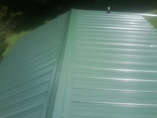 New green metal panels meeting at the ridge of a roof — Flat Roof Repair work by our crew in Rock Hill