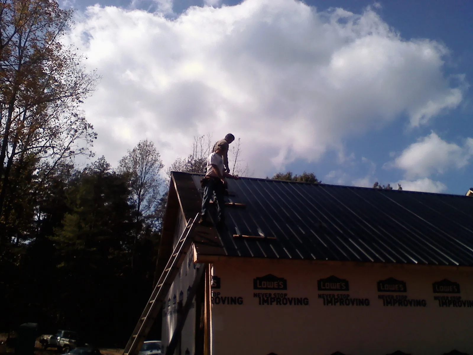 Roofer fastening dark metal panels high against a cloudy sky, from a Roof Inspection job in Rock Hill